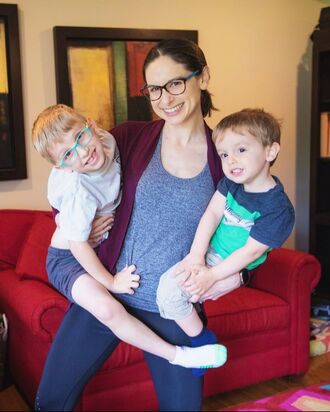 Photo of Tori holding both her sons in front of a red couch
